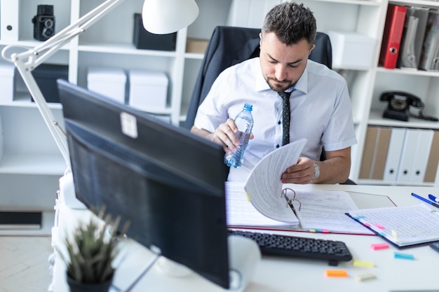 Photo a man is sitting at a table in the office, working with documents and holding a bottle of water in his hand.