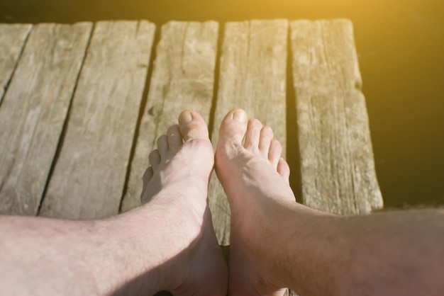 Man is sitting on the wooden pier Rustic and natural photo outdoors Summer river Legs close up