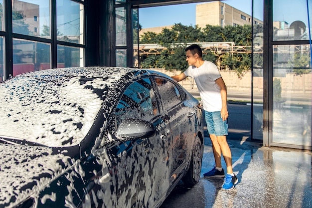 A man is sponging foam on his car at a selfservice car wash station