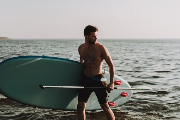 Man Is Standing On The Beach With Surf.