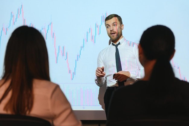 Man is standing near projector and showing graphs and business graphs