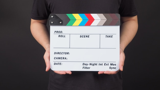 A man is standing with hands is holding Clapperboard or movie slate.It is black background.