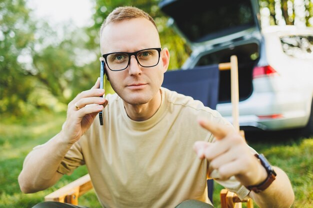 A man is talking on a smartphone while sitting on a bench in a city park A young guy reads the news writes a message on his mobile phone Recreation in nature remote work on vacation