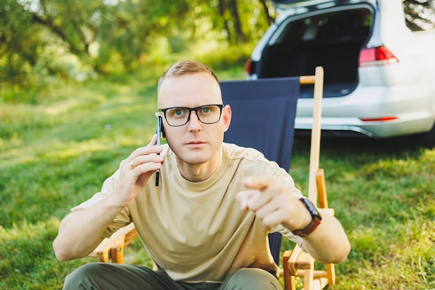 A man is talking on a smartphone while sitting on a bench in a city park A young guy reads the news writes a message on his mobile phone Recreation in nature remote work on vacation