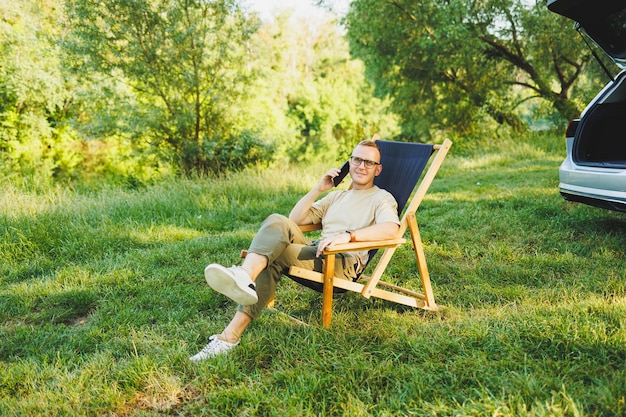 A man is talking on a smartphone while sitting on a bench in a city park A young guy reads the news writes a message on his mobile phone Recreation in nature remote work on vacation