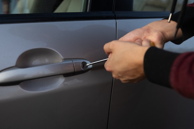 A man is trying to break the car lock in order to steal it from the parking lot.