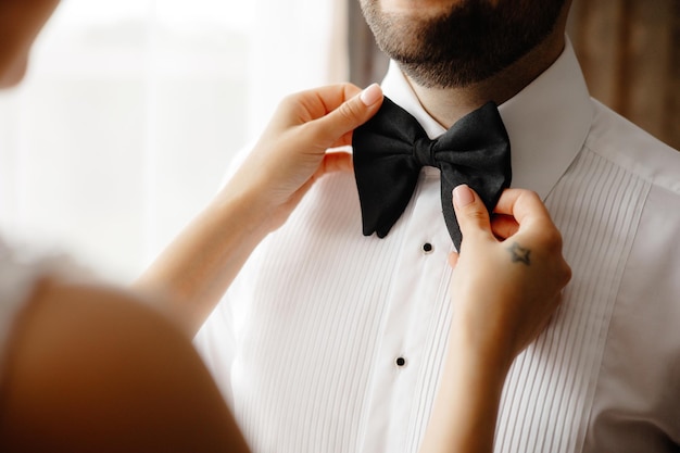 Photo a man is tying a bow tie with a woman in the background.