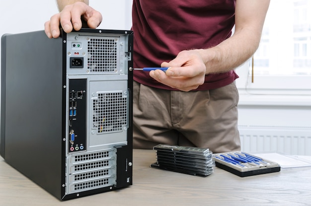 A man is unwinding the screw for access inside the desktop.