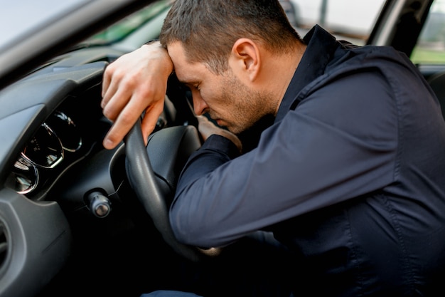 The man is very tired of driving a car and sleeping on the steering wheel