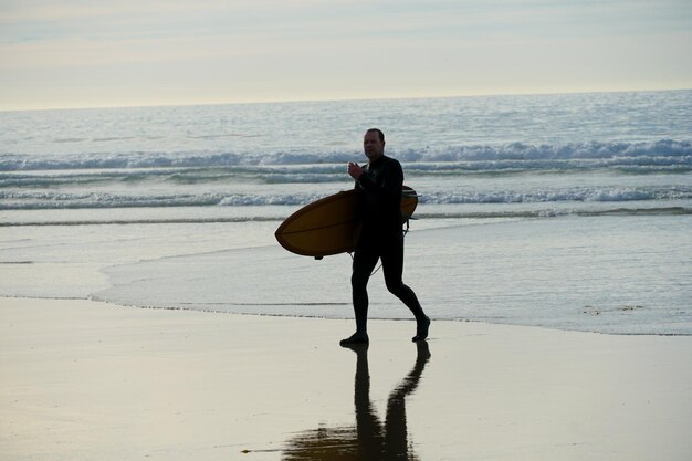 A man is walking on the beach with a surfboard.