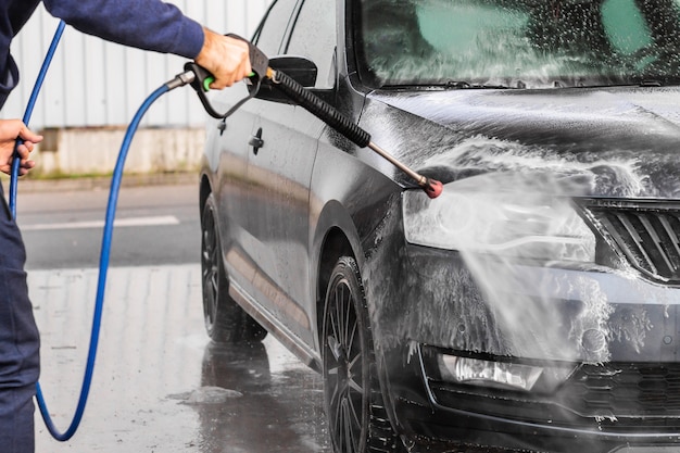 A man is washing a car at self service car wash. High pressure vehicle washer machine sprays foam