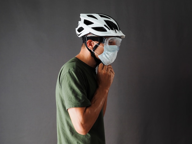 The man is wearing a green t-shirt, face mask and protective goggles, fasteners bicycle helmet.