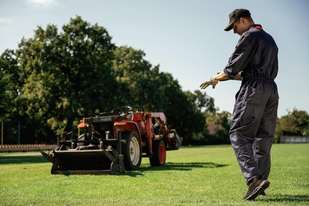 Man is with utility tractor with grass cutter and aerator equipment on the field