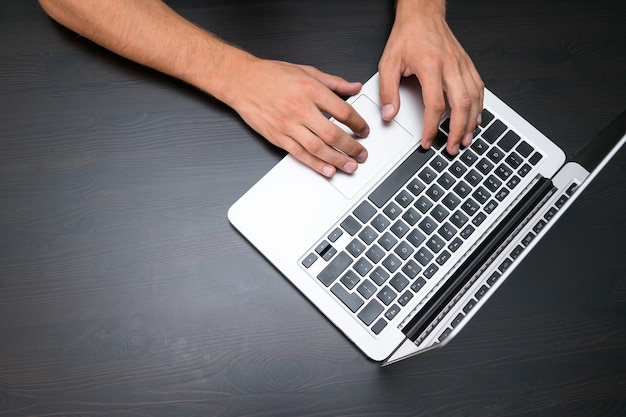 A man is working by using a laptop computer on vintage wooden table. Hands typing on a keyboard. Top view, business office workplace