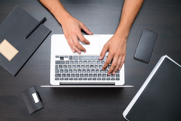 A man is working by using a laptop computer on vintage wooden table. Hands typing keyboard.