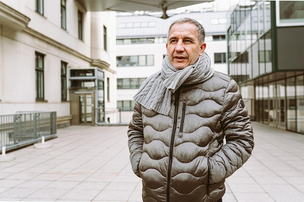 A man in a jacket and scarf walks down a street.