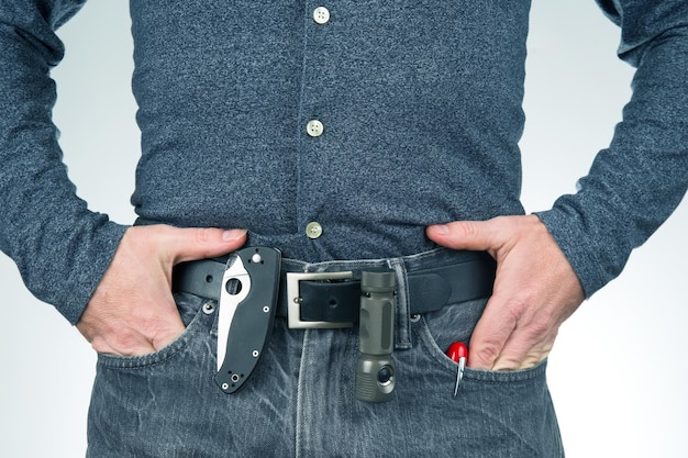 Man in jeans on a leather belt with a flashlight and a knife survival items