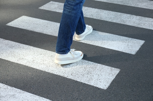 Man in jeans and sneakers walking on crosswalk.