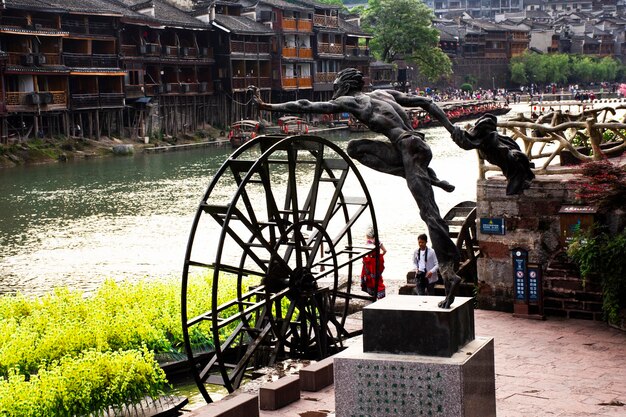 Photo man jump statue to tuojiang river in historical building heritage architecture of xiangxi phoenix ancient city or antique old town fenghuang for chinese travelers visit on may 9 2024 in hunan china