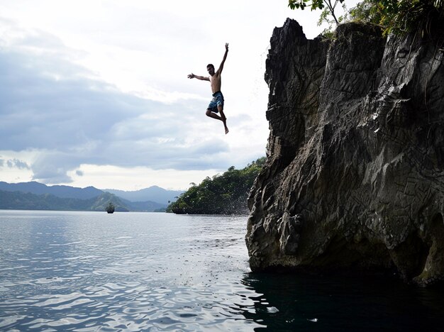 Photo a man jumping off a cliff into the water