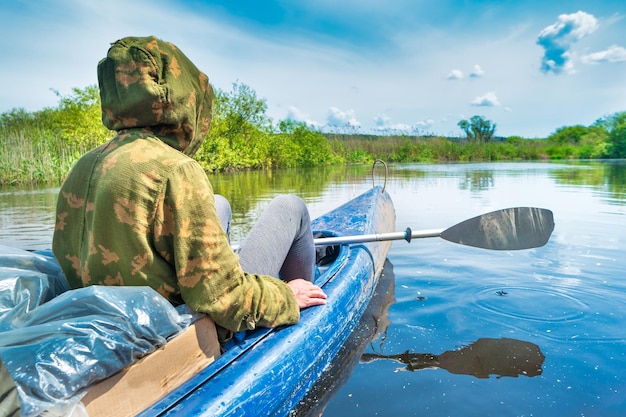 Man at kayak trip on blue river landscape and green forest with trees blue water clouds sky