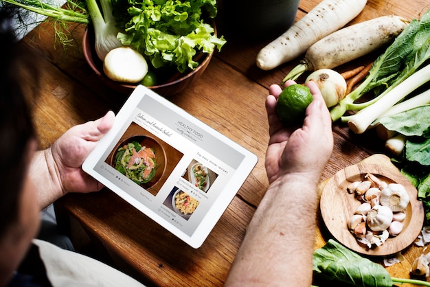 A man in a kitchen holding a fresh bergamot and reading a recipe of healthy food