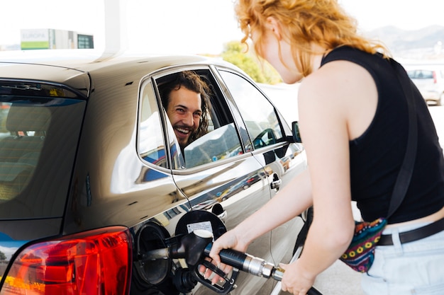 Man laughing out of car window with woman filling up car 