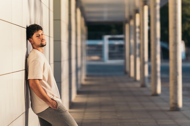 Man leaning on a facade while facing the camera outdoors during sunset