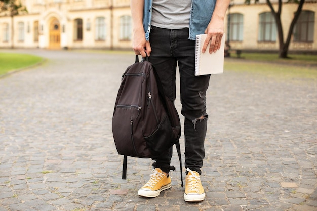 Man legs in yellow sneakers, wearing grey shirt, black skinny jeans at university campus in autumn