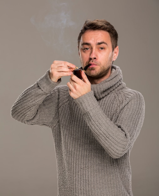 man lights a pipe with a match in the studio on a gray background