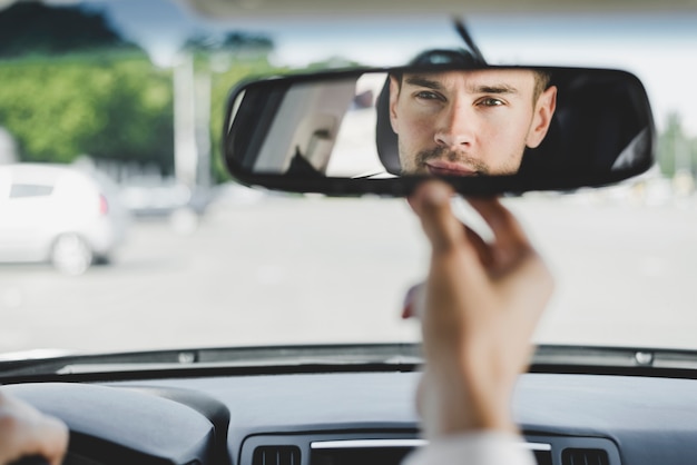 Man looking back through the rear view mirror from the front seat of a car