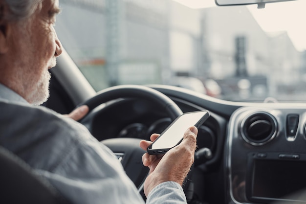 Man looking at mobile phone while driving a car. Old pensioner person distracting texting and chatting.