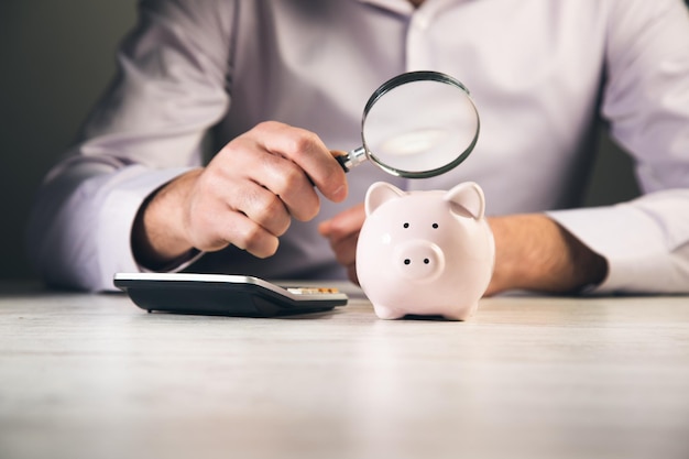 Man looking at piggy bank throught magnifying glass Concept of FinancexDxA