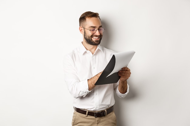 Man looking satisfied while reading documents, holding clipboard and smiling, standing over white background.