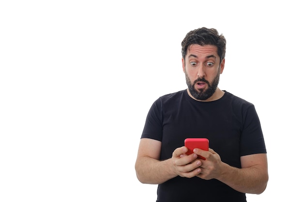 Man looking surprised at his mobile phone while standing on an isolated background. Technology and communication concept.