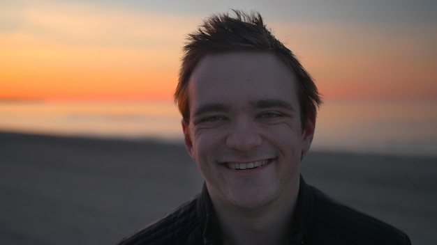 A man looks at the camera against the backdrop of a sunset and smiles