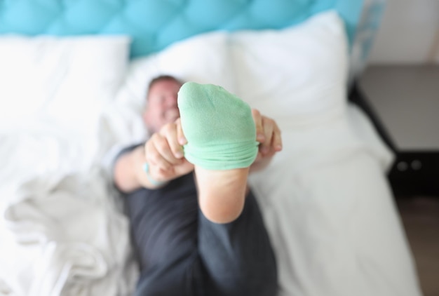 Man lying on bed and putting on green sock closeup