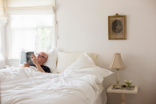 Man lying in a bed with white linen reading