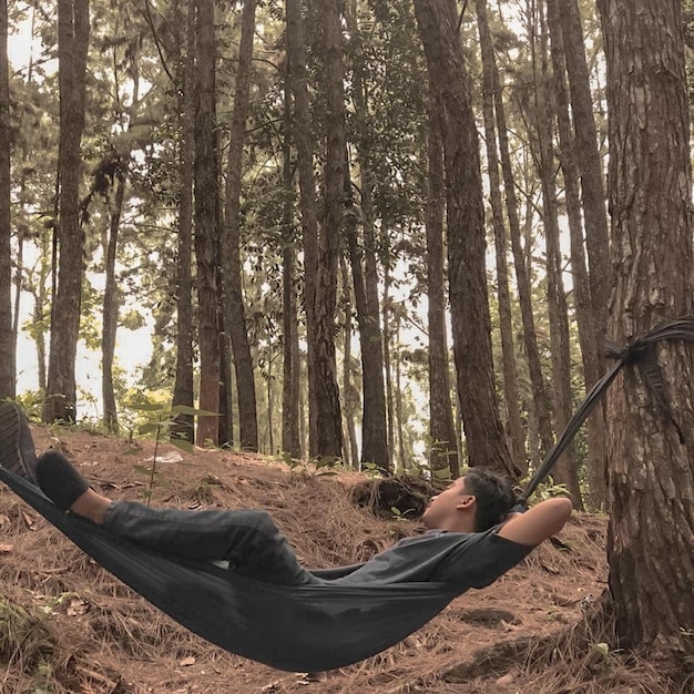 Photo man lying down on land against trees in forest