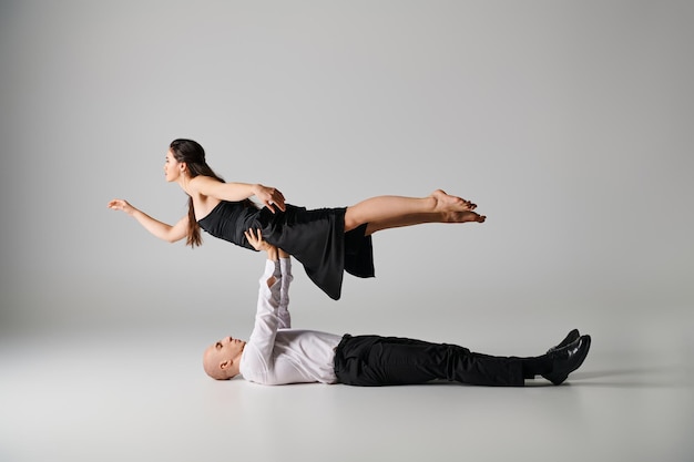 man lying on the floor and lifting body of woman in dress during dance performance on grey backdrop