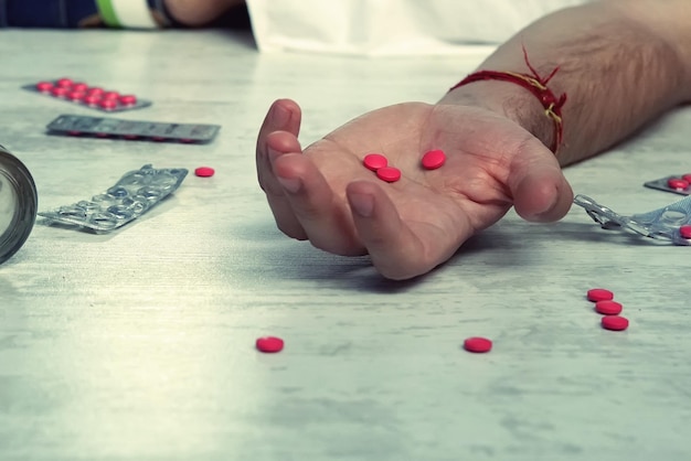 A man lying unconscious from an overdose of pills red tablets in the hand of a young man concept of suicide poisoning from pills drug overdose