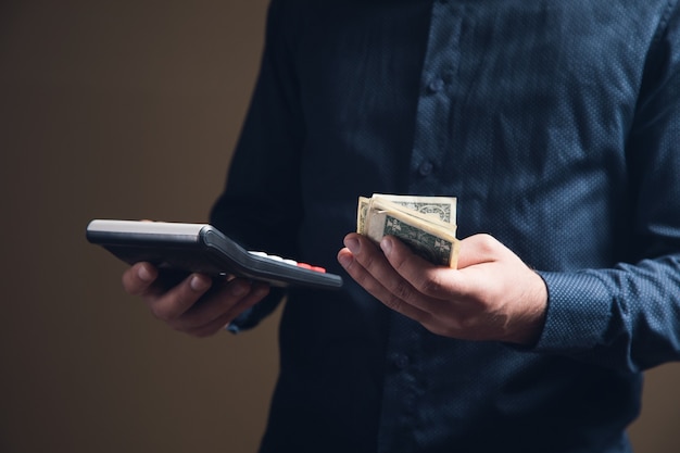 A man makes calculations on a cooler and holds money on a brown surface