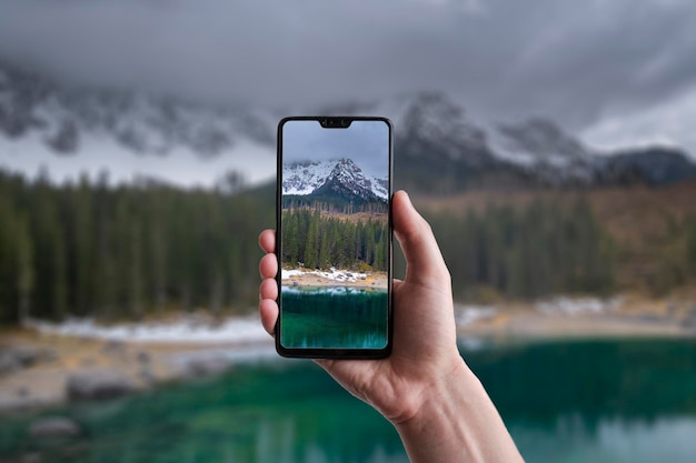 A man makes a photo on a smartphone beautiful landscape of Lake Carezza with Mount Latemar Bolzano province South tyrol Italy