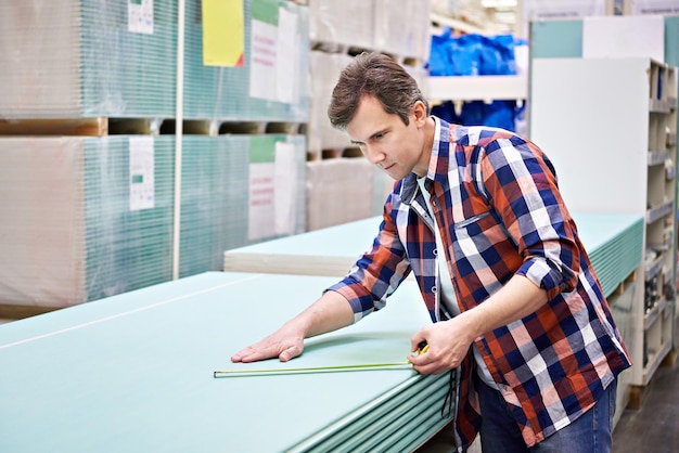 Man measures with roulette drywall sheets in store building materials