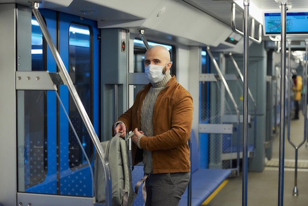 A man in a medical face mask to avoid the spread of coronavirus is putting on a backpack