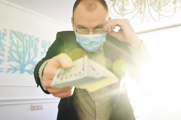 A man in a medical mask holds a pack of one hundred dollar bills in his hands The economic growth