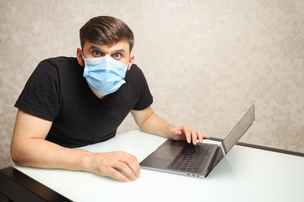 a man in a medical mask on selfisolation works at a laptop