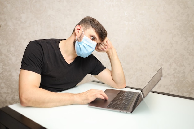 a man in a medical mask on selfisolation works at a laptop