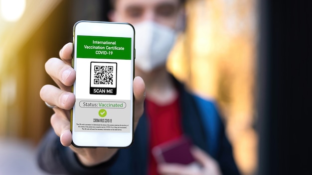 Man in medical mask showing an International Vaccination Certificate COVID-19 QR code on smartphone