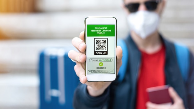 Man in medical mask showing an International Vaccination Certificate COVID-19 QR code on smartphone